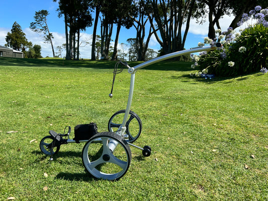 Golf push cart on a grassy field with trees and flowers in the background